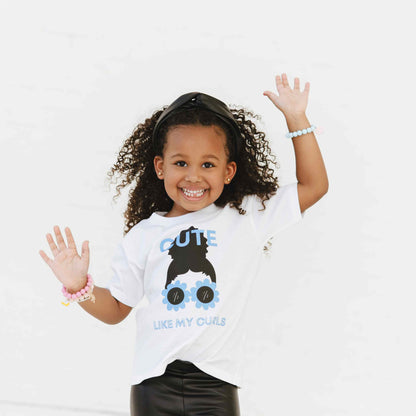 A child wearing a white t-shirt with a graphic print of a character resembling a girl with curly hair and sunglasses.