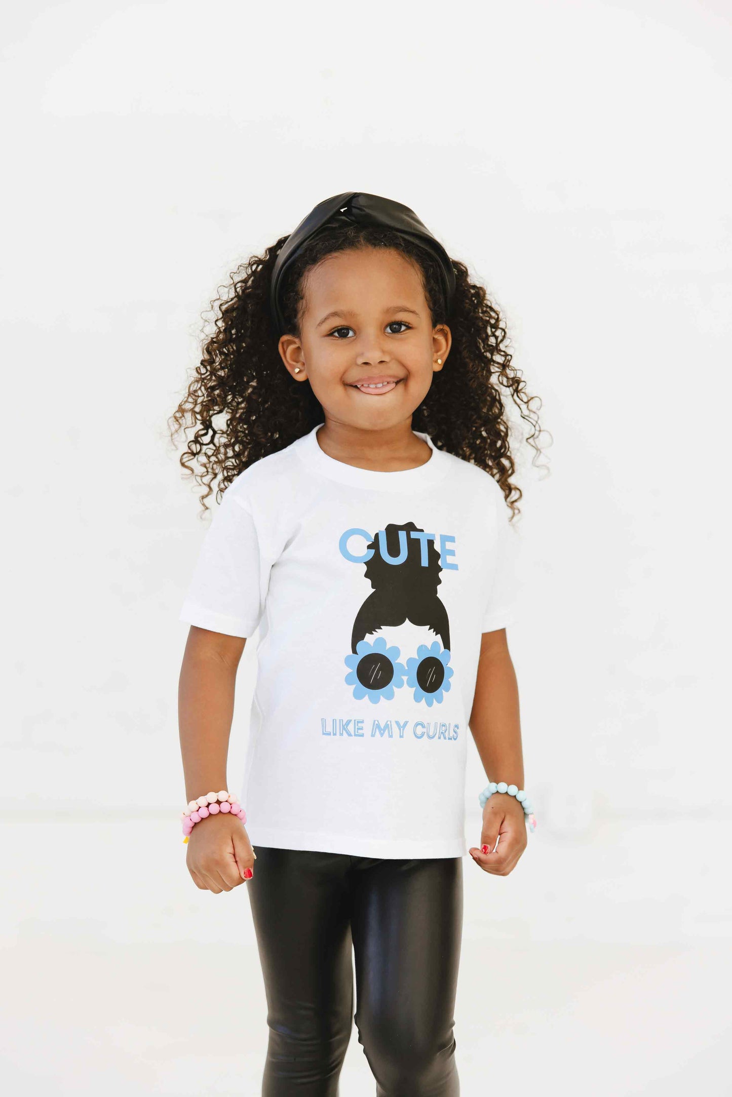 A child wearing a white t-shirt with a graphic print of a character resembling a girl with curly hair and sunglasses.