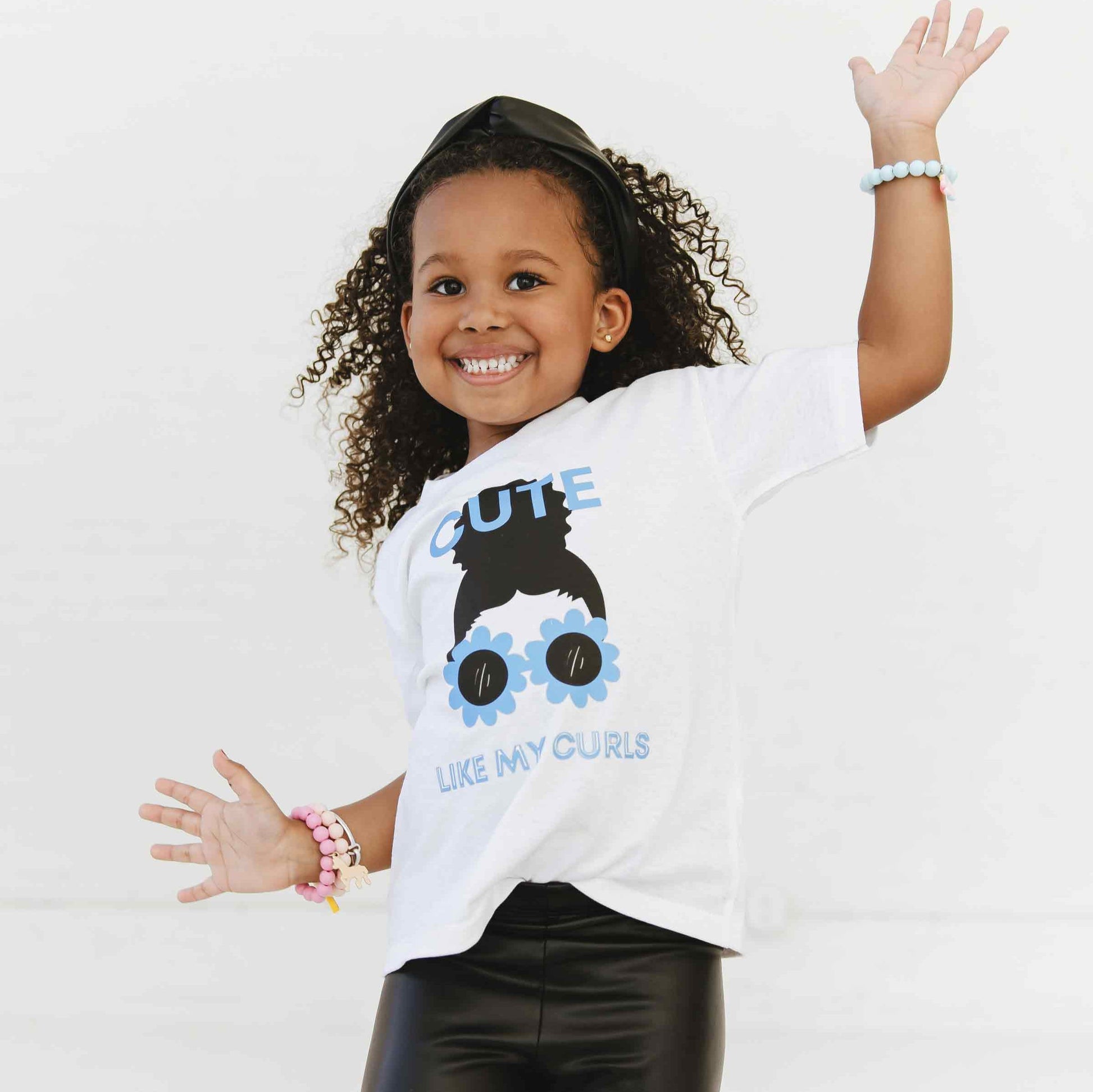 A child wearing a white t-shirt with a graphic print of a character resembling a girl with curly hair and sunglasses.