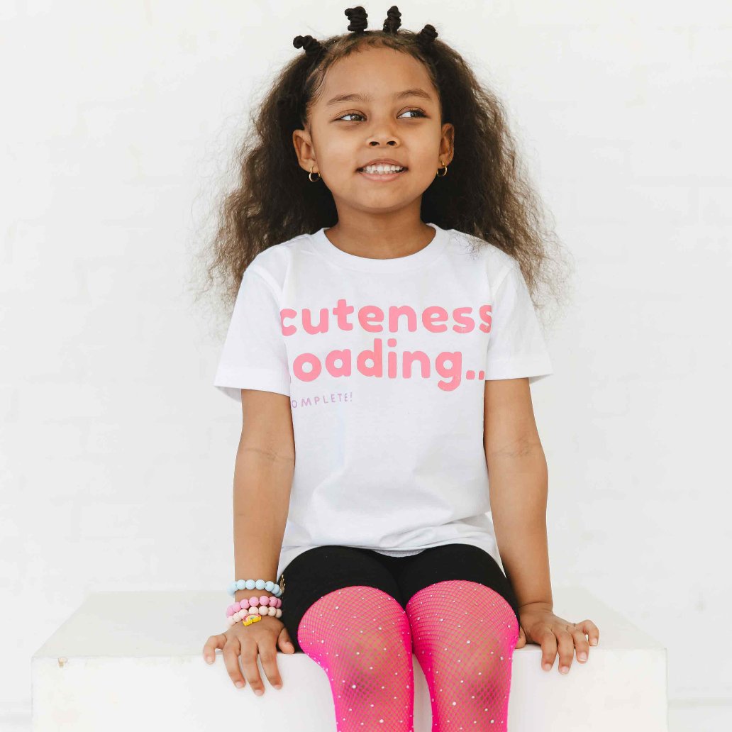 A child wearing a white t-shirt with a graphic word  print saying "Cuteness Loading".