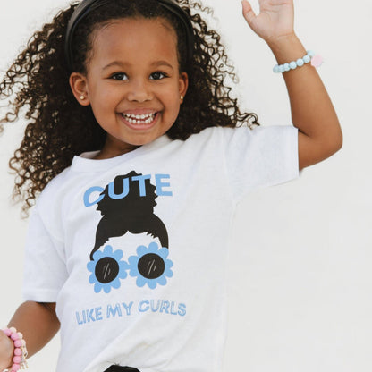 A child wearing a white t-shirt with a graphic print of a character resembling a girl with curly hair and sunglasses.