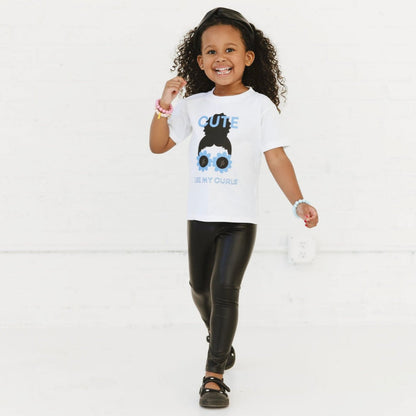 A child wearing a white t-shirt with a graphic print of a character resembling a girl with curly hair and sunglasses.